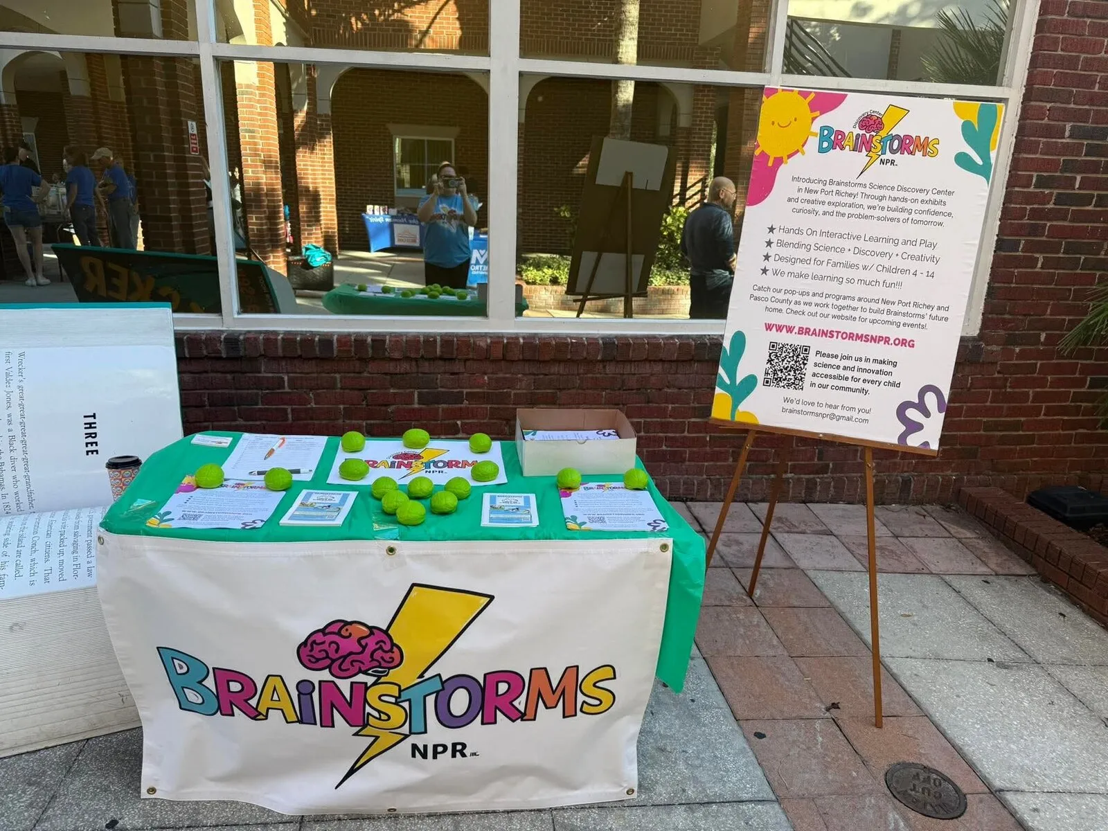 A Brainstorms popup table with banner, activity balls and an information sign on a downtown sidewalk