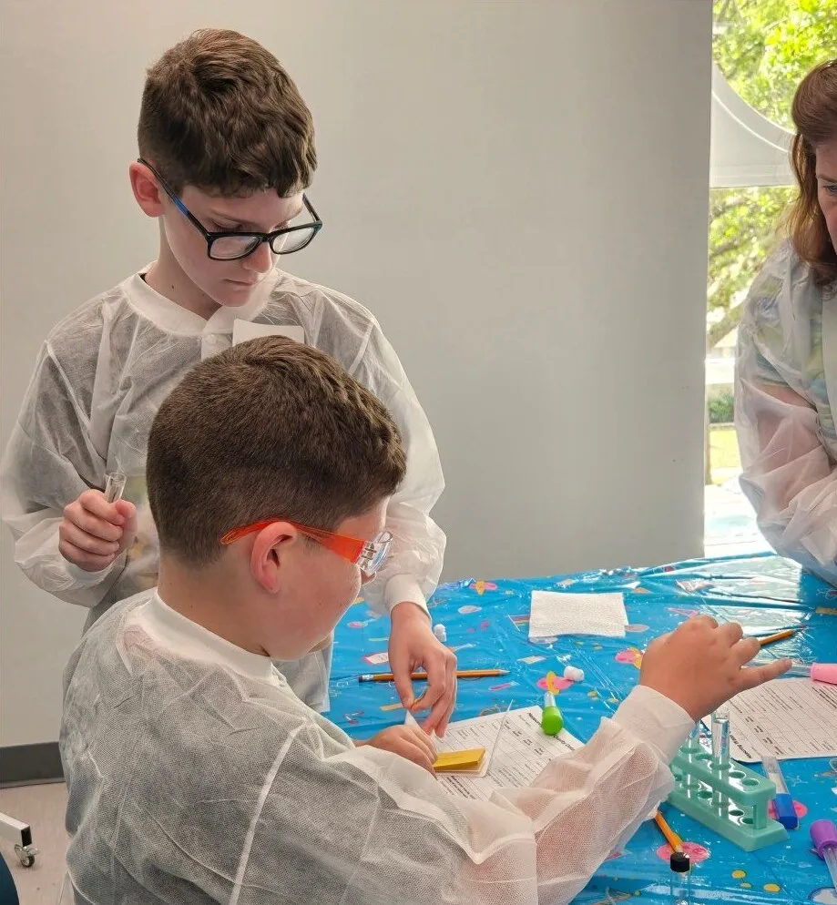 A student in a red cap and lab coat works on an experiment at a Science Saturday