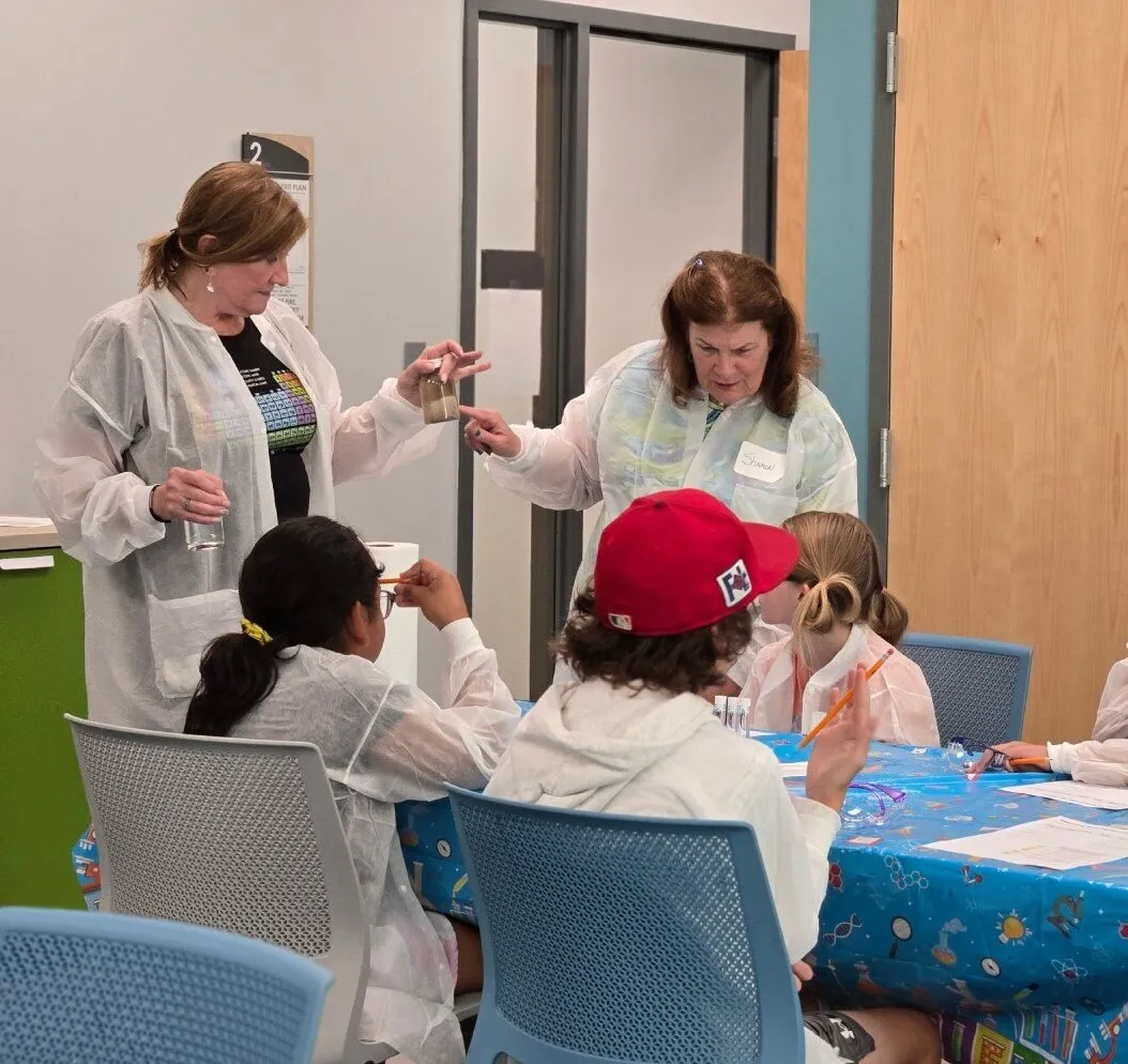 Students in lab coats explore materials together at a Science Saturday